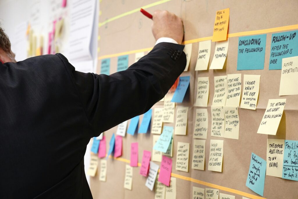 Project manager placing multiple sticky notes on a whiteboard, organizing and coordinating several projects and tasks simultaneously in an office setting.