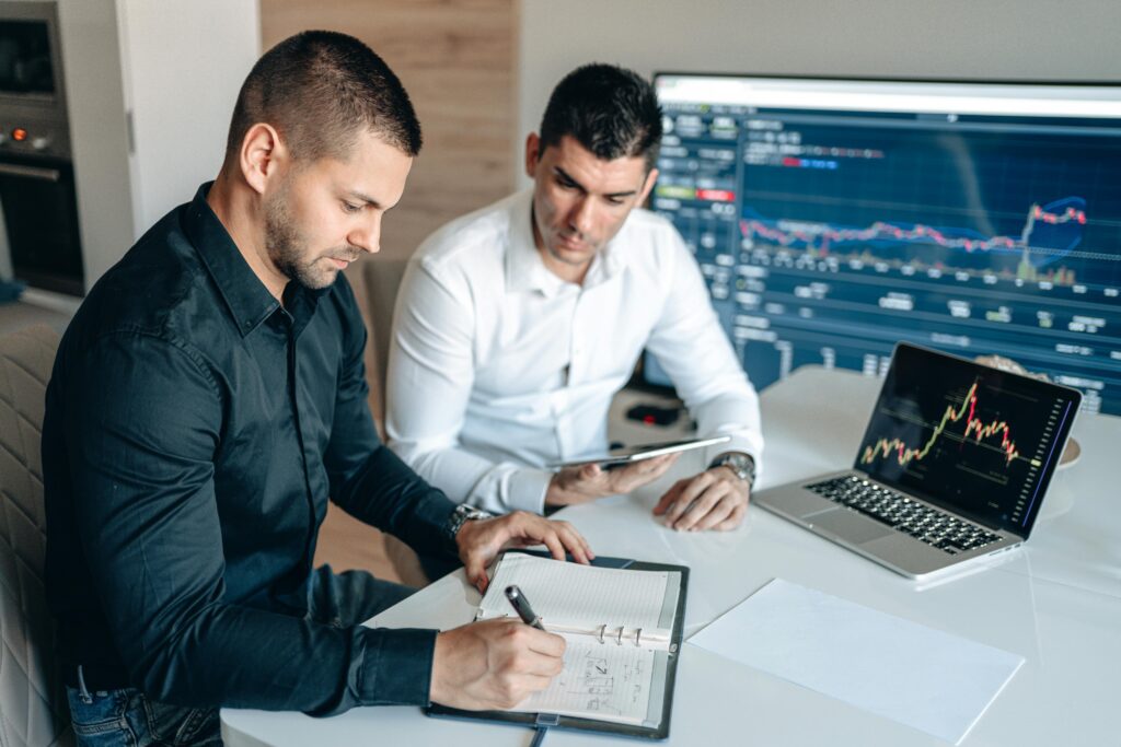 Data analyst recruiters reviewing financial data dashboards and charts on laptop screens while analyzing reports and taking notes in a modern office setting