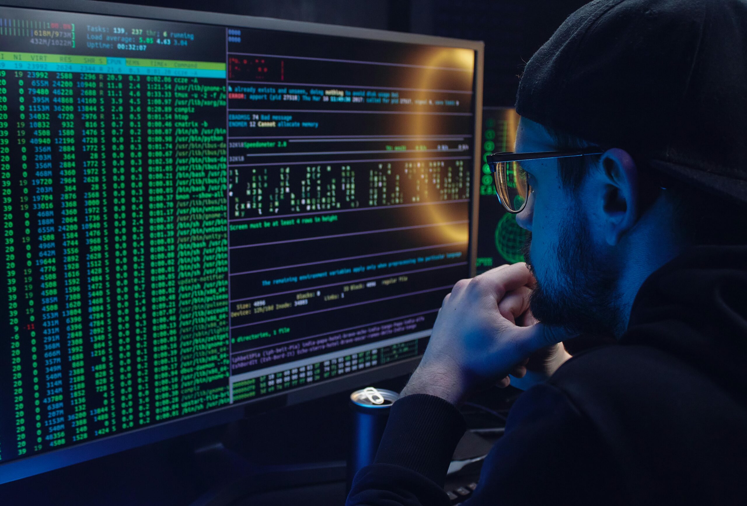 Cybersecurity analyst monitoring code and security systems on multiple computer screens